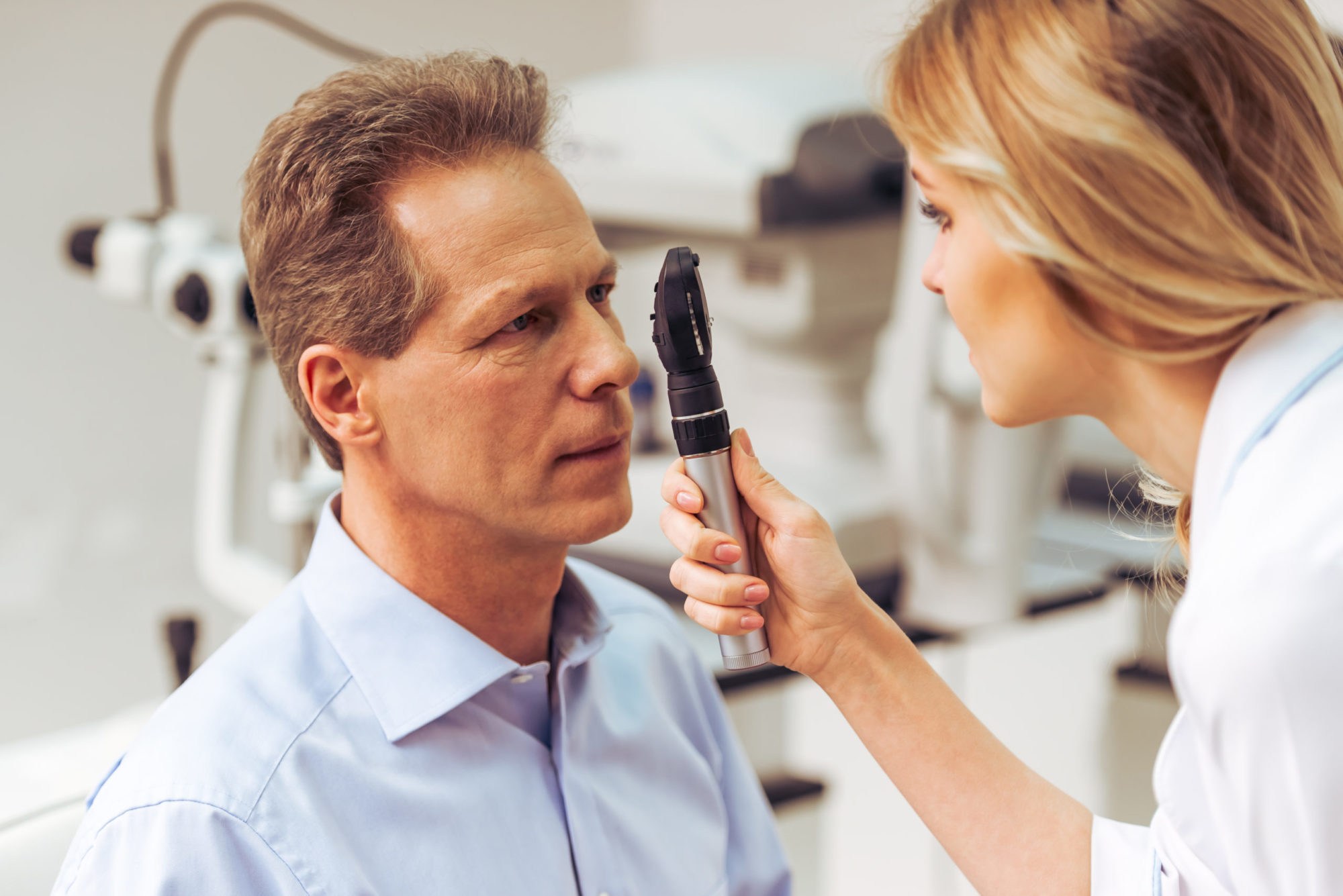 Young beautiful female ophthalmologist examining handsome middle aged man with modern equipment,close-up